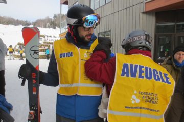 Une vue de dos d’un participant avec la main sur l’épaule d’un guide tenant des skis. – à Val Saint-Côme.