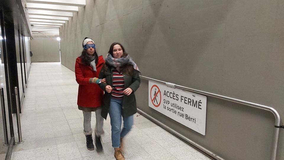 une femme accompagne une autre femme portant un bandeau sur les yeux dans le métro lors de la formation des monitrices et des moniteurs en 2019.