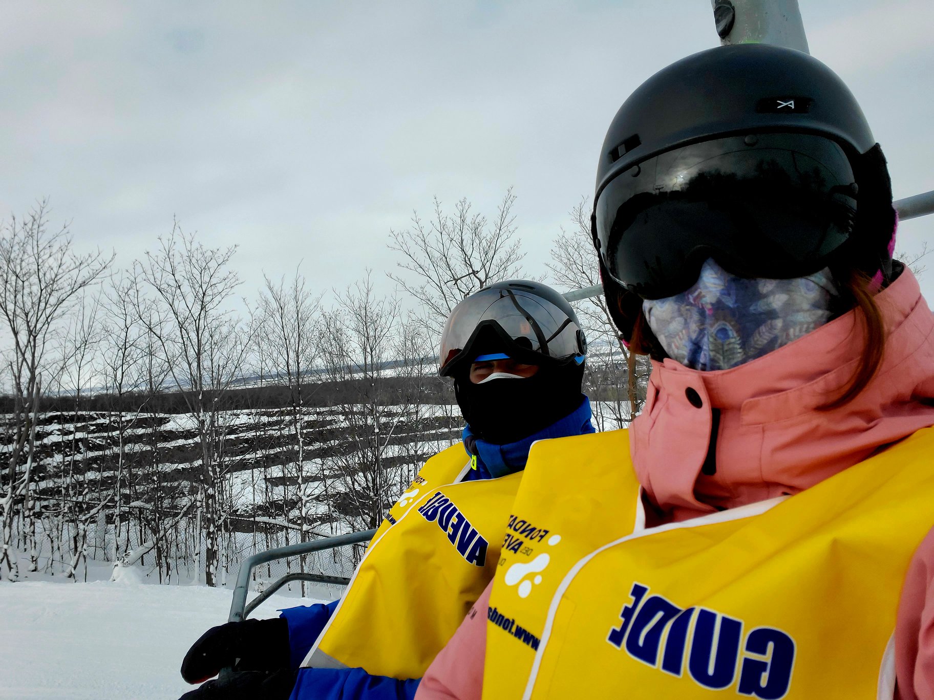un égoportrait d’une accompagnatrice et d’un participant dans un remonte-pente lors d’une sortie de ski. Les deux individus portent un couvre-visage. Voir moins — partage une actualité COVID-19.