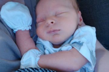 Un bébé naissant dort avec des gants protecteurs sur les mains.