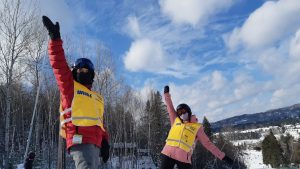 Un participant et une guide font une pose devant la caméra en ayant chacun le bras droit levé.