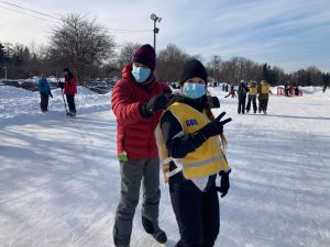 Une accompagnatrice regarde vers la caméra en faisant un signe de paix avec ses doigts alors qu’un participant se tient derrière elle en lui tenant les épaules.