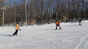Une guide en ski à reculons observe un participant descendant la pente.