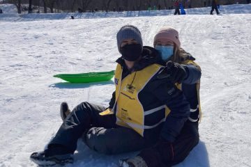 Une accompagnatrice pointant vers la caméra est assise avec un participant dans la neige.