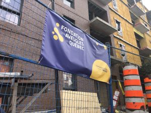 Une bannière de la FAQ est posée sur une barrière de métal lors de la construction de l’immeuble au 9050 Sherbrooke Est.