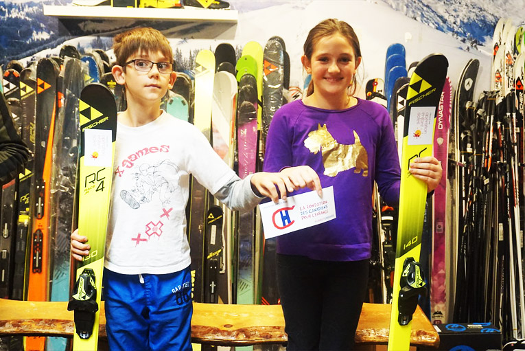 Des participants lors de l'essayage de skis tenant fièrement les logos d'Opération Enfant Soleil et Fondation des Canadiens pour l'enfance dans leurs mains.
