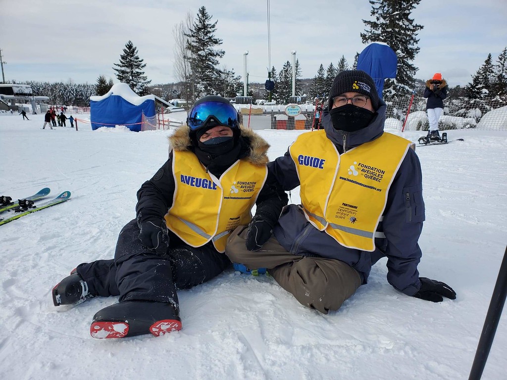 Description de l'image: Un moniteur et un participant portant les dossards de la Fondation assis dans la neige au mont St-Sauveur.