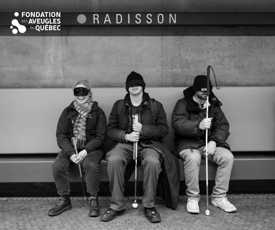 Photo en noir en blanc de trois moniteurs les yeux bandés assis sur un banc à l'intérieur du métro Radisson. Ils sourient, une canne blanche à la main.