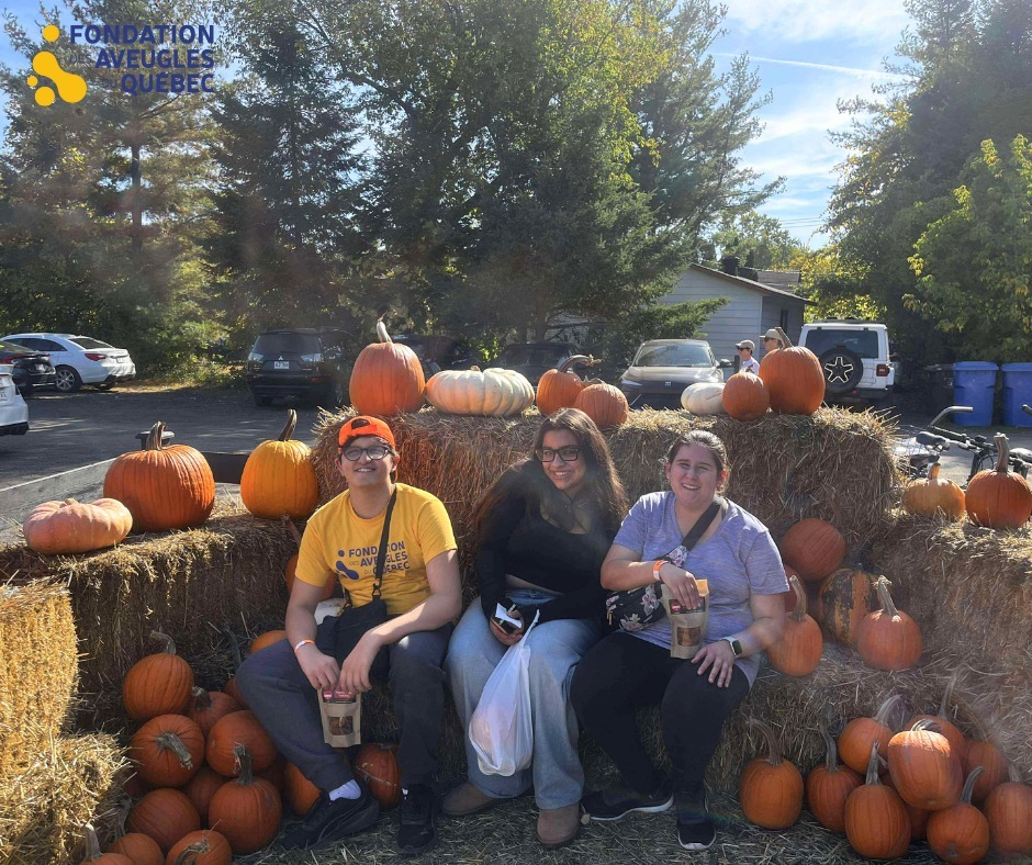 photo de deux jeunes avec une monitrice. ils sont assis dans une botte de foin avec des citrouilles orange autour d'eux.