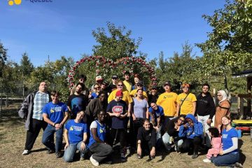 photo de groupe lors de la cueillette de pomme. derrière eux, il y a une arche en forme de coeur avec des fleurs.